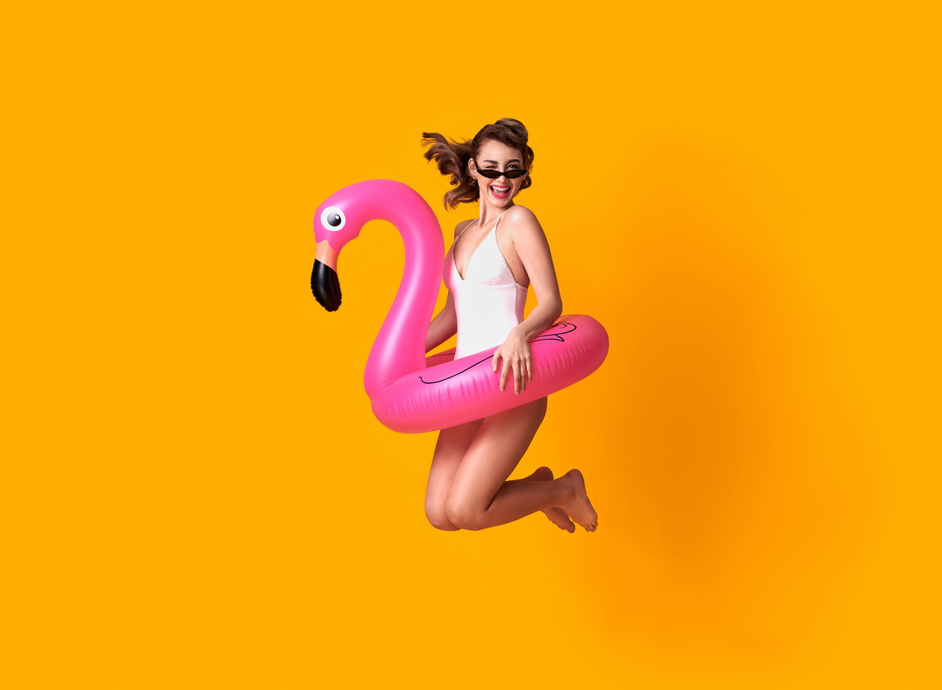 happy-young-woman-jumping-on-yellow-wall-dressed-in-swimwear-holding-flamingo-rubber-ring-beach.jpg
